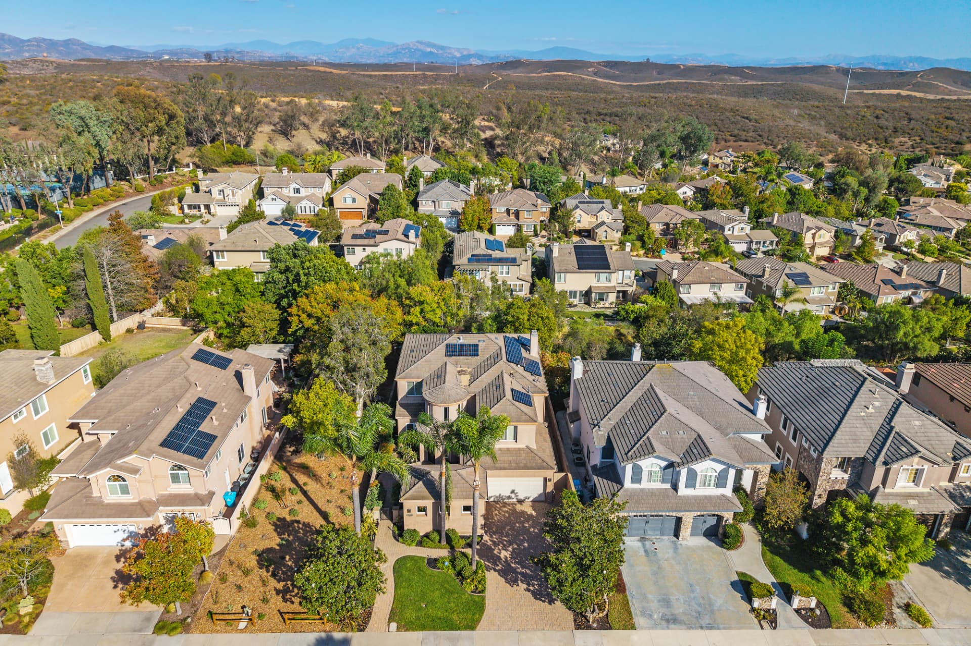 Aerial of a suburban neighborhood of two-story homes with solar panels along the edge of open foothills