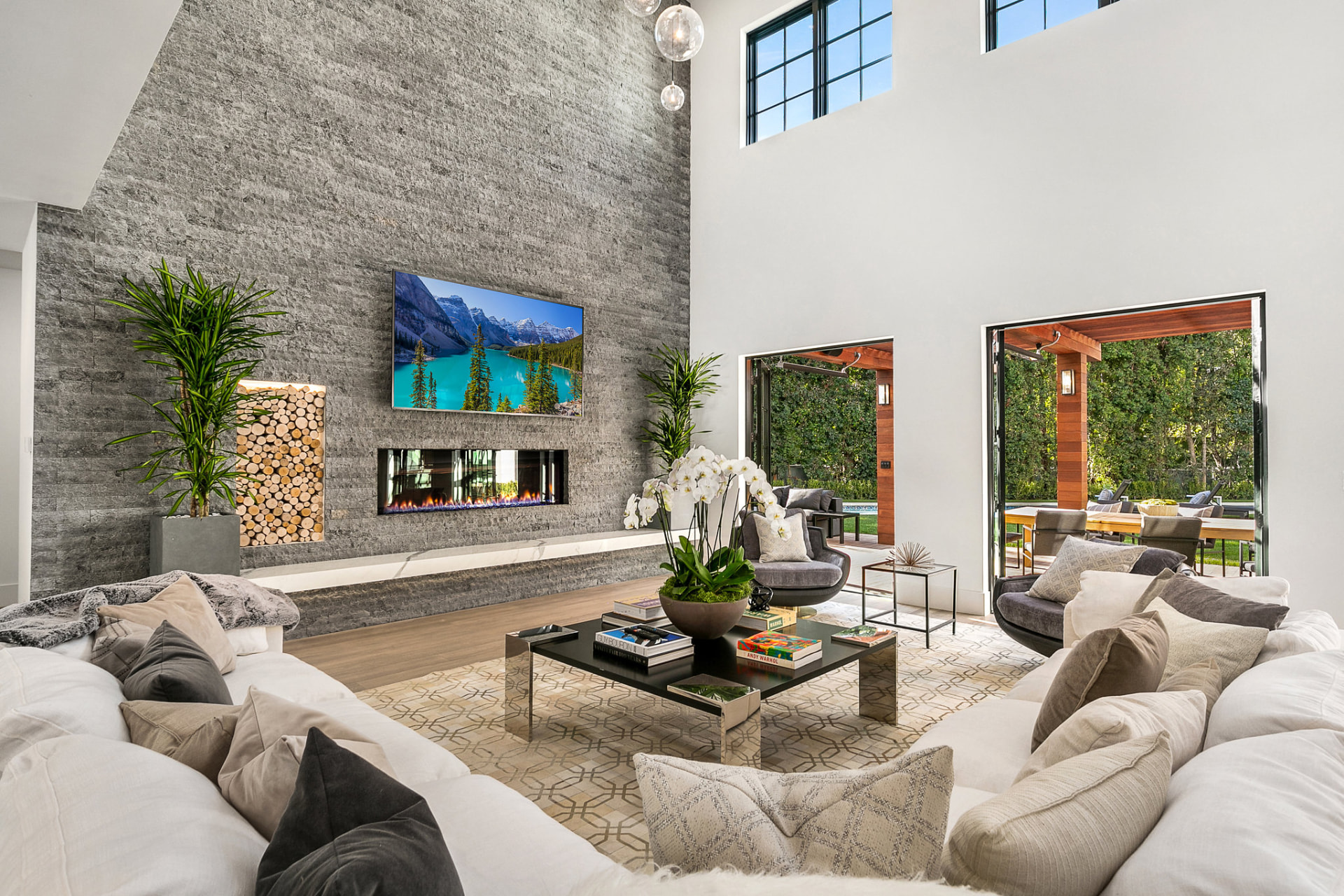 High-ceiling living room with a stone fireplace opening to the patio