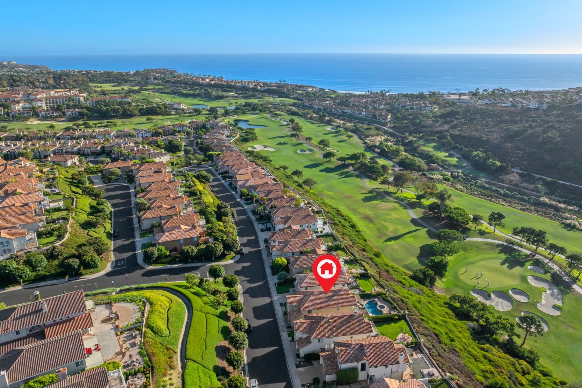 Aerial view of a Mediterranean home bordering a golf course with ocean views beyond