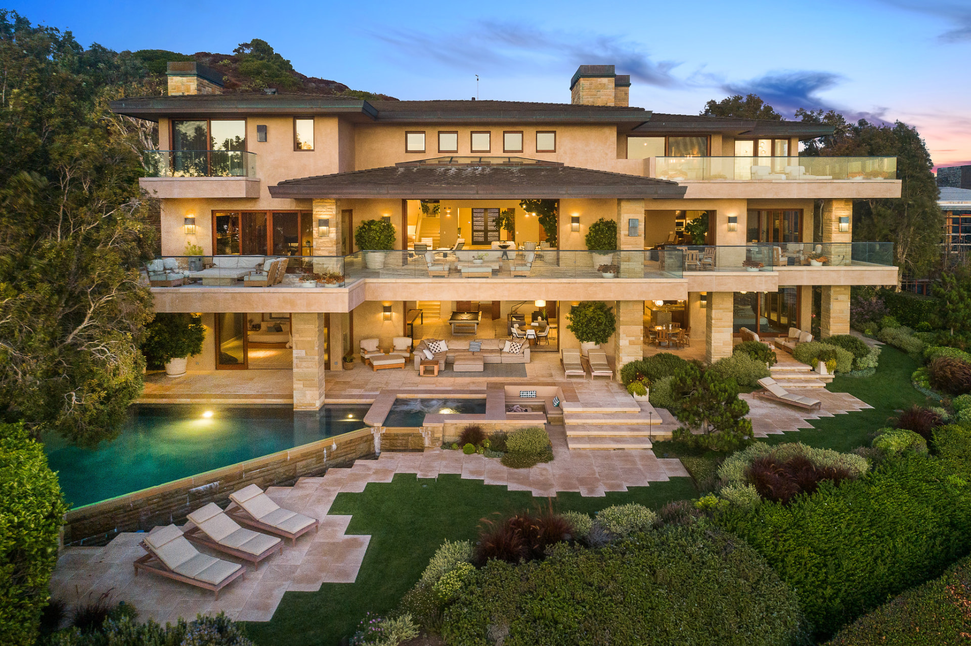Multi-level estate with an illuminated pool and stone patios at twilight