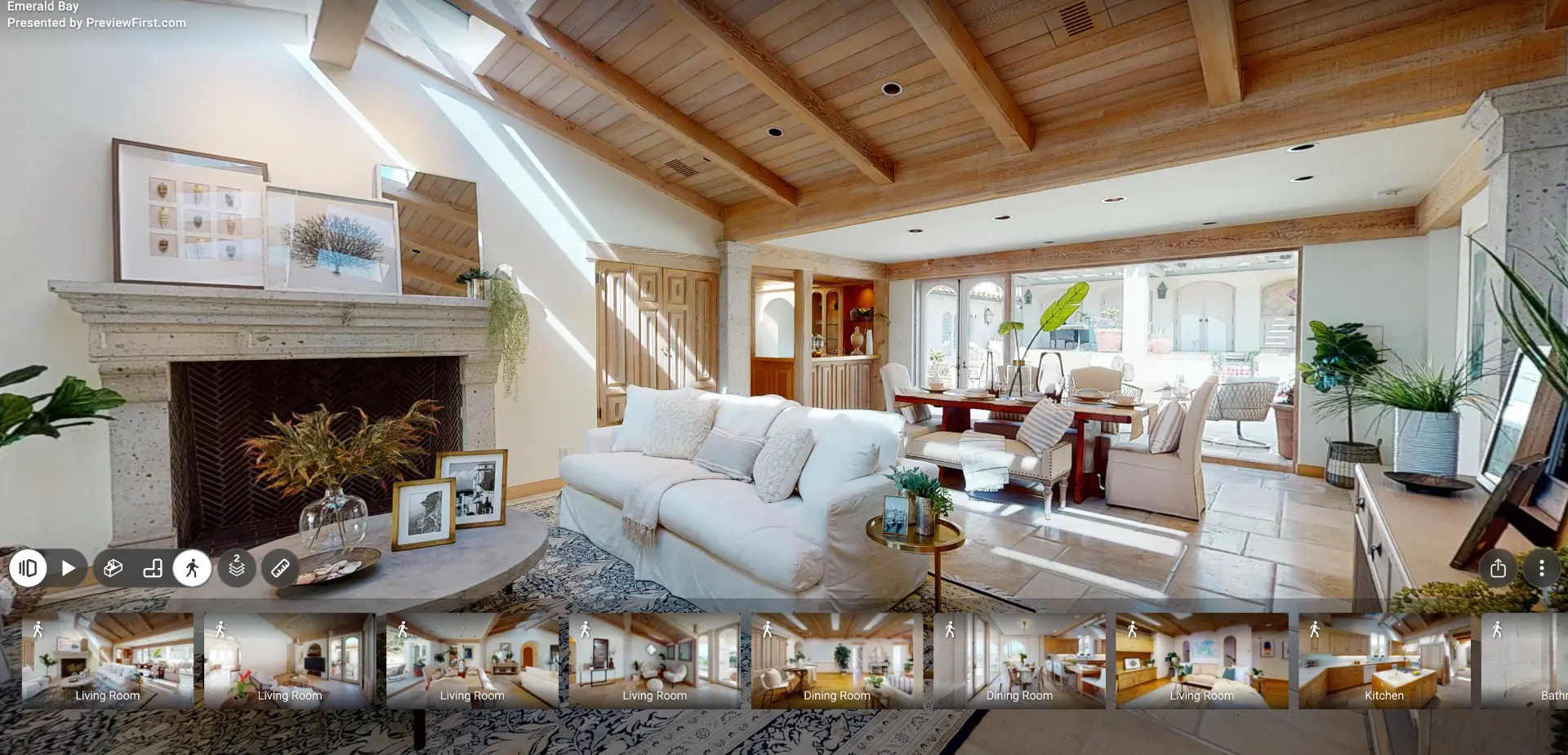 Matterport 3D tour of a sunlit living and dining room with exposed wood beams, a stone fireplace and tile floors