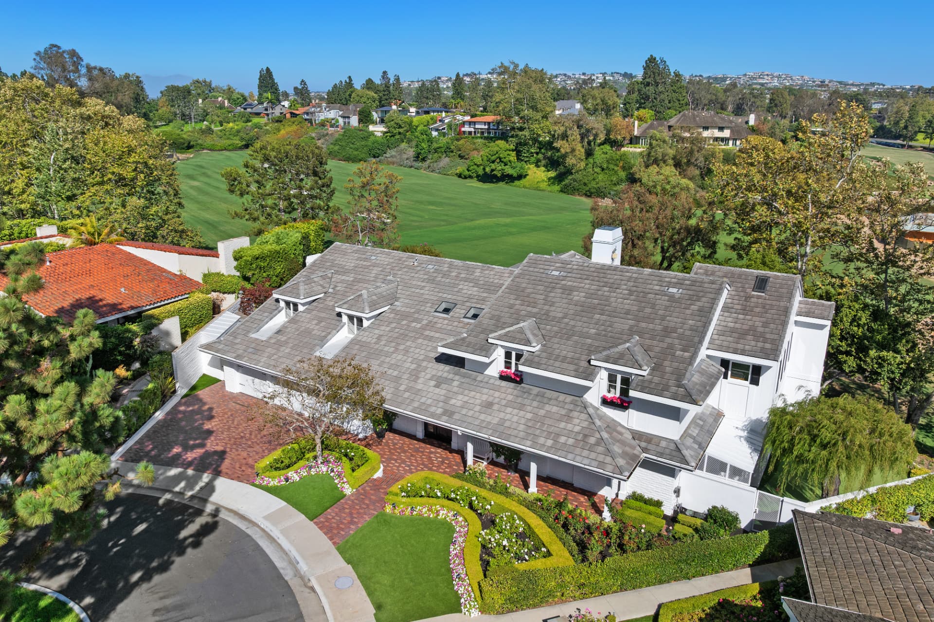 Aerial of a white multi-story home with a brick driveway bordering a golf course fairway